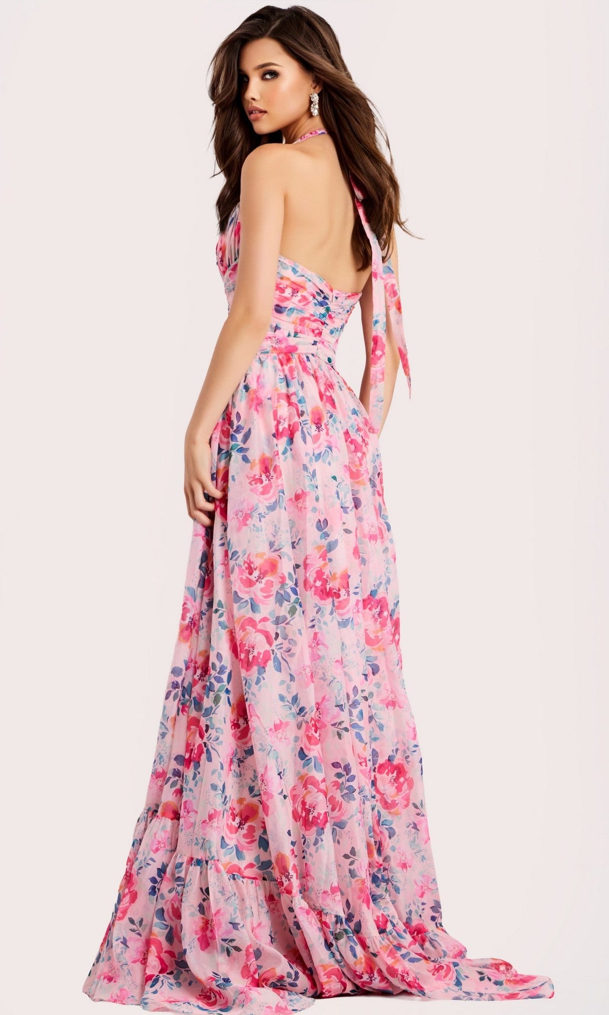 A woman models the Jovani 48469, a long, sleeveless pink floral halter prom dress with an open back, standing against a plain light background.